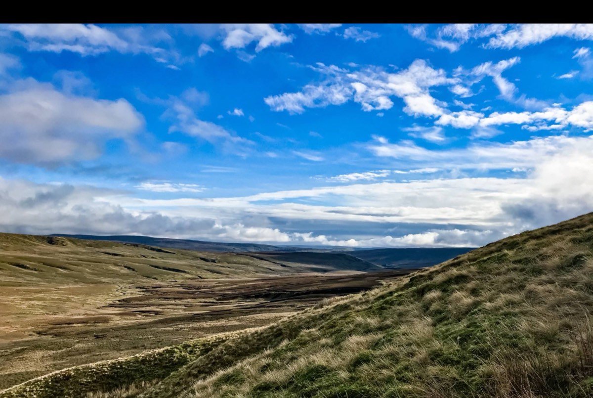 A wide moorland valley with a bright blue sky and streaks of white cloud.