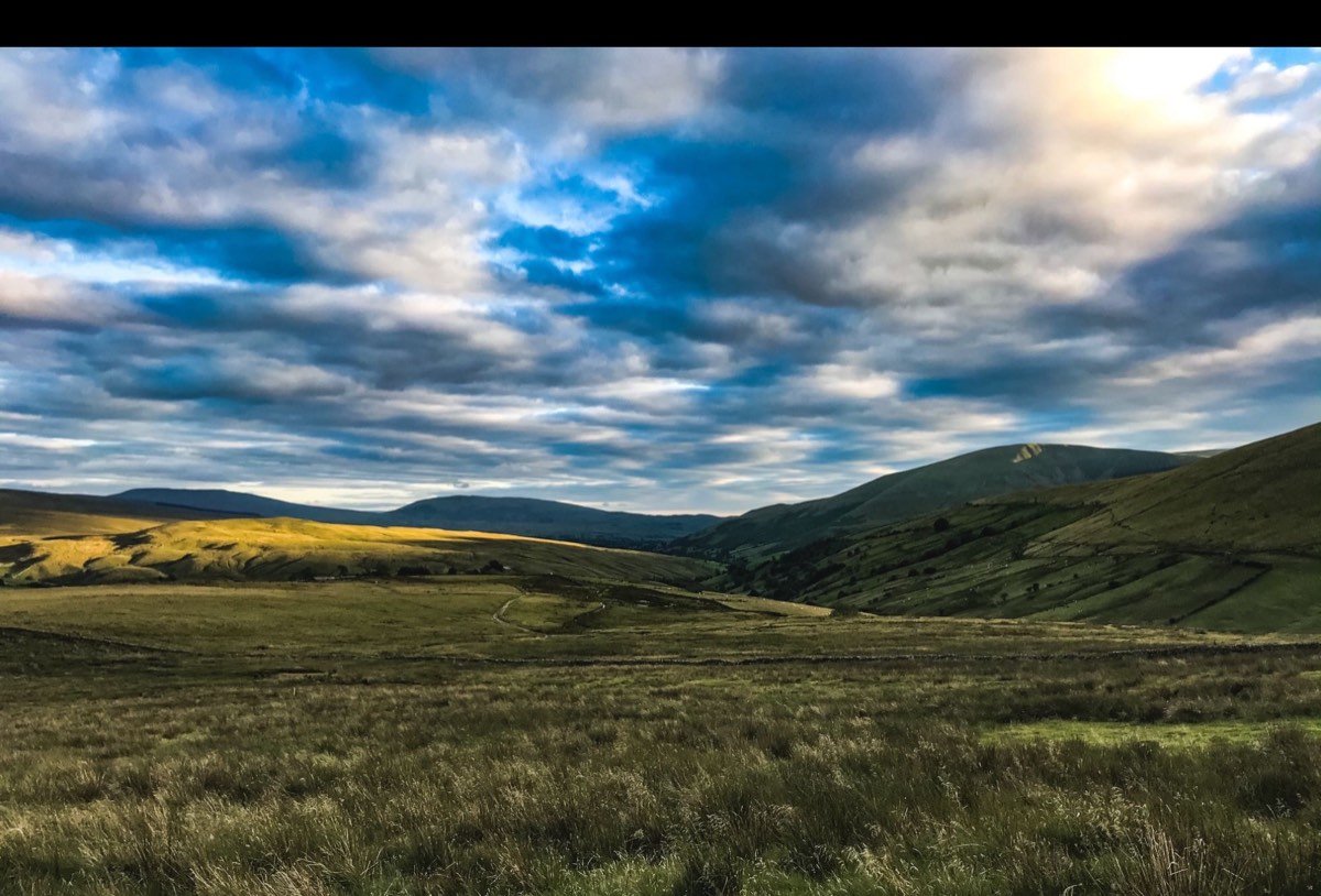 Evening light falling on rolling moorland and a green valley beneath a broken sky.