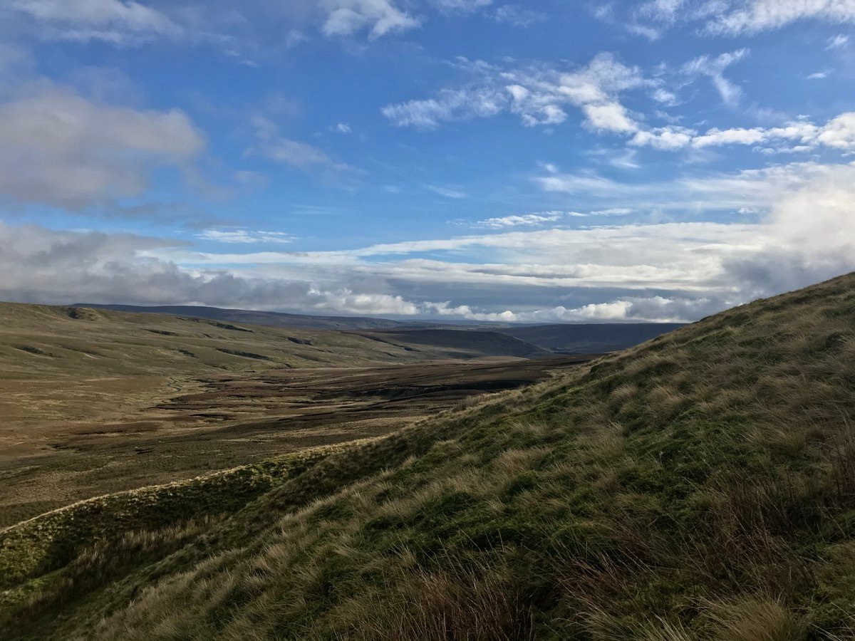 A long grassy moorland valley under broken cloud and blue sky.